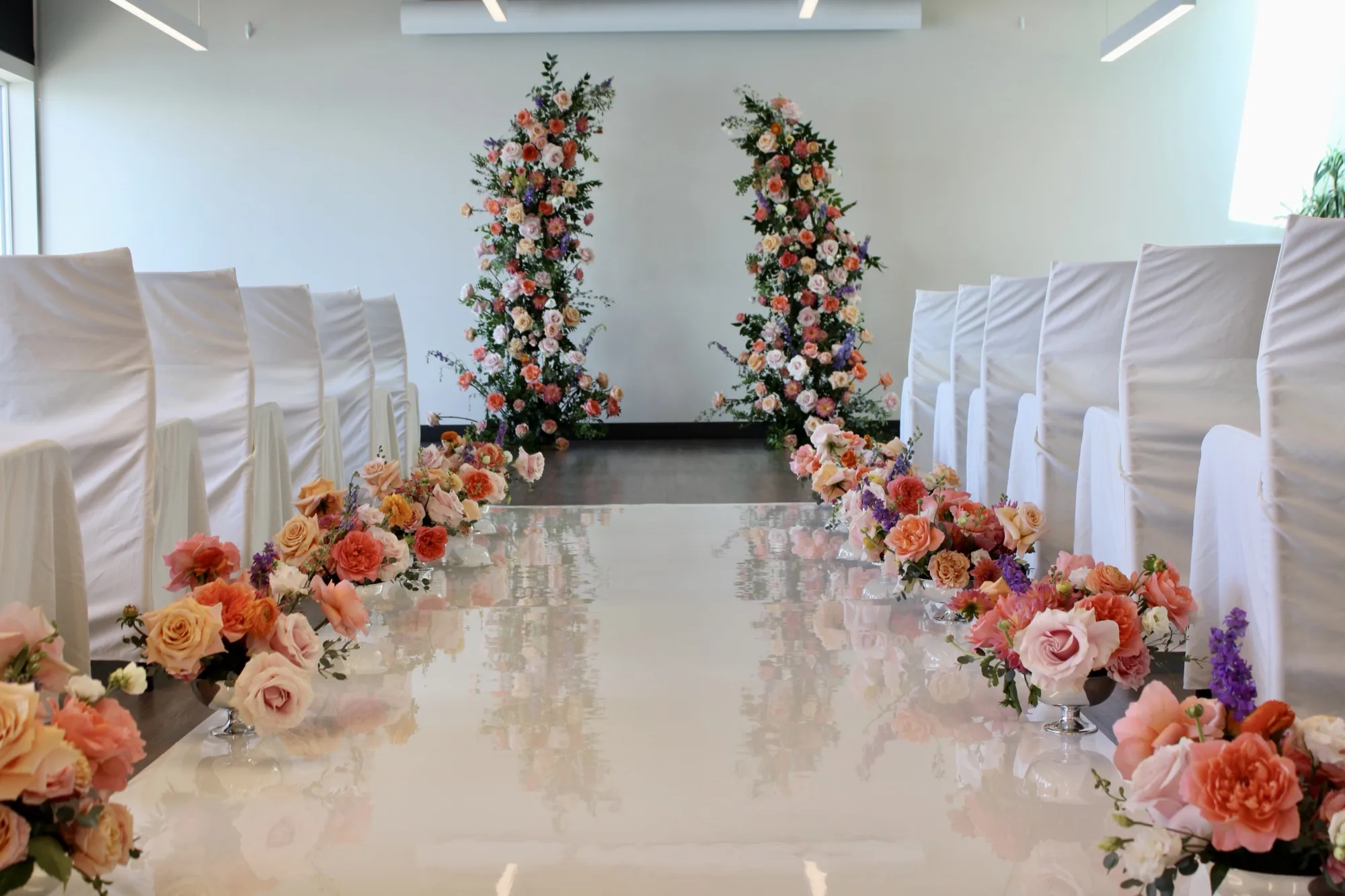 A symmetrical wedding ceremony aisle with peach and coral floral pedestals.